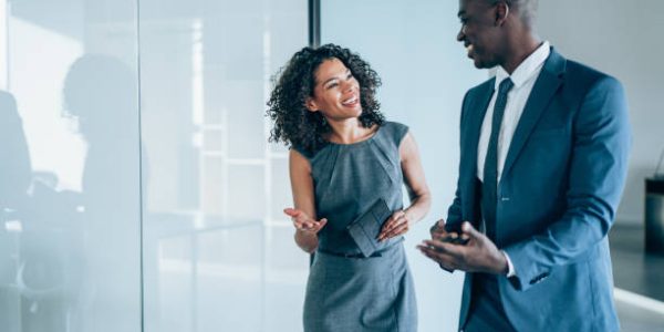 Shot of two young colleagues having a discussion in modern office. Confident young business people working together in the office. Corporate business persons discussing new project and sharing ideas in the workplace.